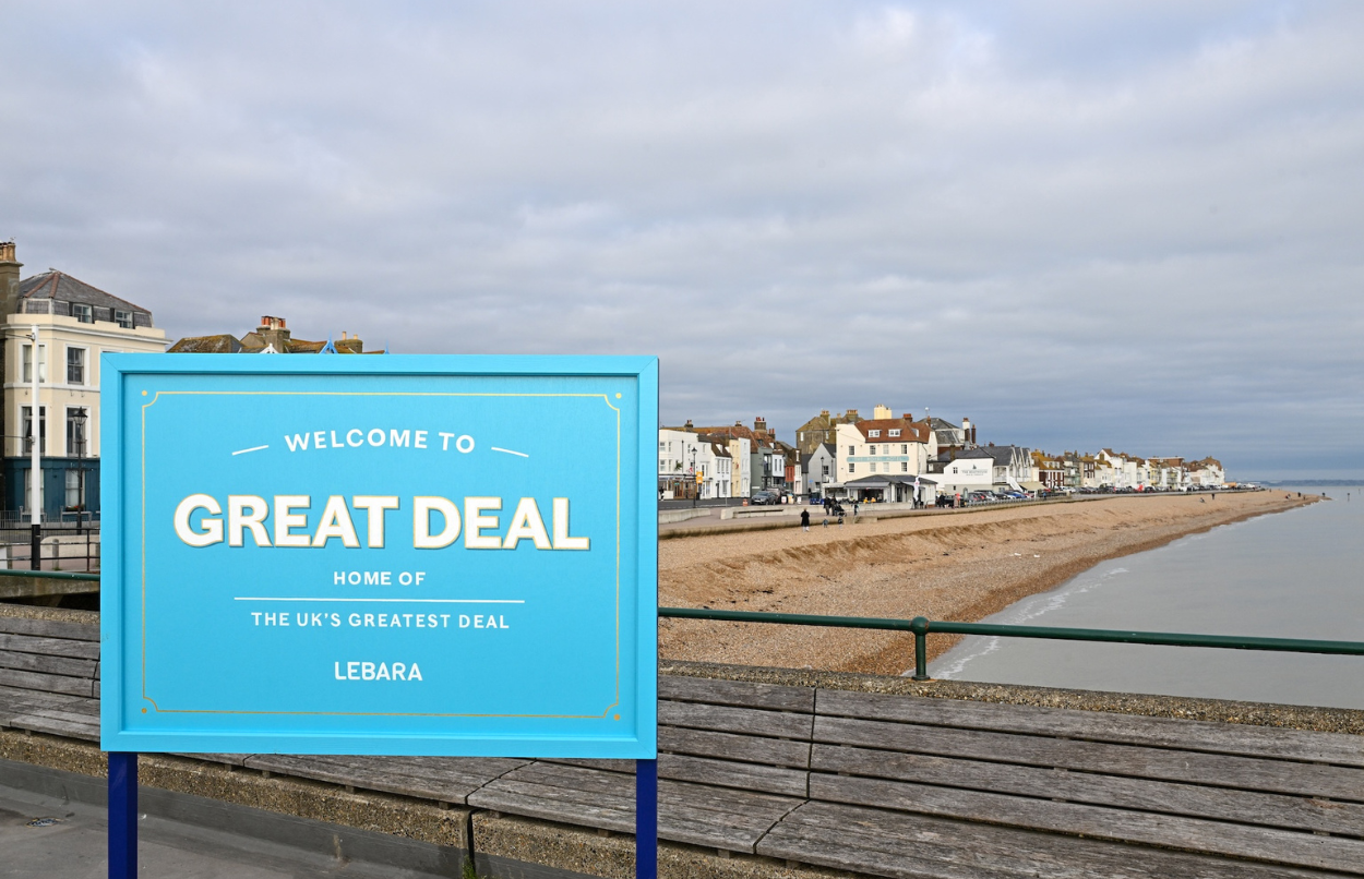 A seaside town with blue board in front of it saying Welcome to Great Deal